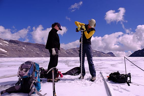 Zwei Personen bohren eine Messtange in die Gletscheroberfläche.